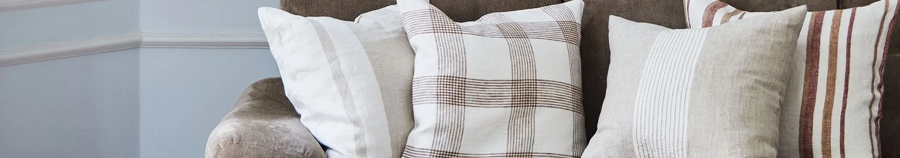 茶色のソファにある3つのクッションのクローズアップ。白、ベージュ、格子柄に茶色と赤のストライプが特徴。