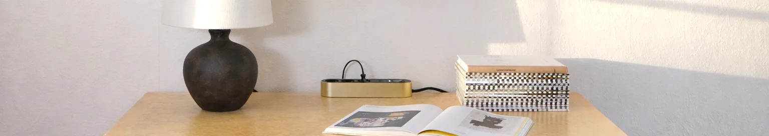 明るい表面に置かれた、3つの黒いコンセントと電源ボタンが付いたゴールドの電源タップ。