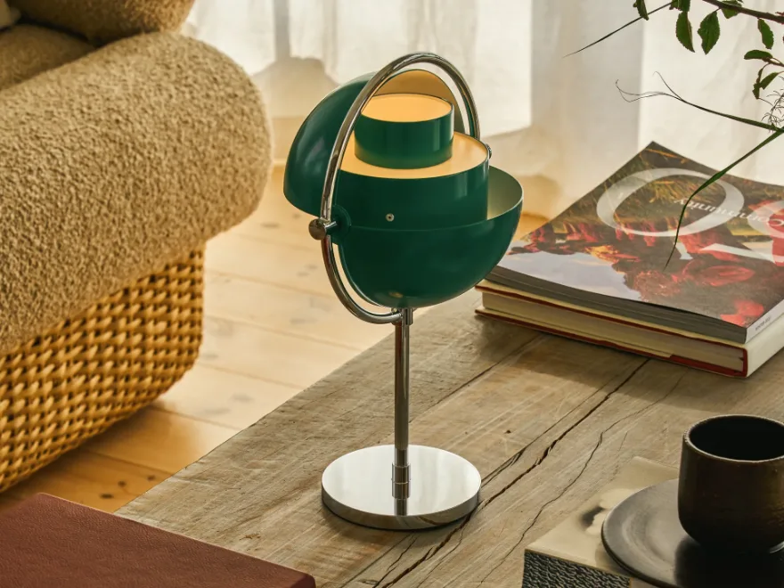 クロームベースと彫刻的な多層シェードを持つ緑色のテーブルランプが、素朴な木製のコーヒーテーブルに置かれている。