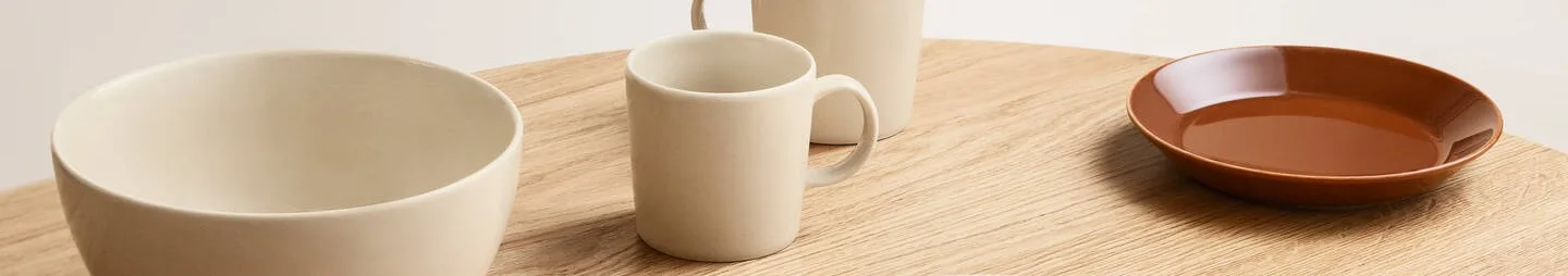 クリーム色のボウルとマグカップ、そして薄い木製テーブルに置かれた茶色の皿。