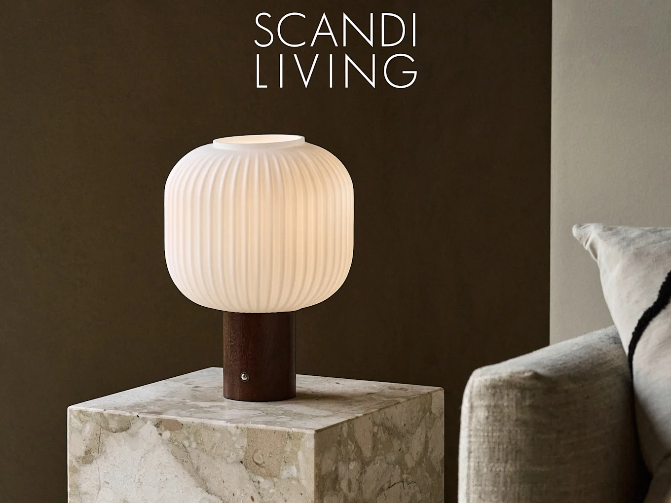 白い縦溝入りガラスシェードと濃い木製台座のテーブルランプが大理石のテーブルに置かれ、背景は暗い壁。「SCANDI LIVING」の文字。