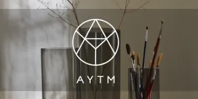 透明な花瓶にドライフラワー、絵筆立てに絵筆が入っており、AYTMのロゴが見える。