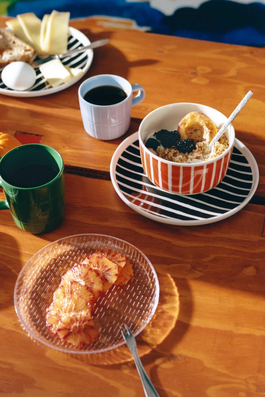 木製テーブルに朝食、ストライプの食器、コーヒー、オートミール、チーズ、パン、卵、ブラッドオレンジスライス。