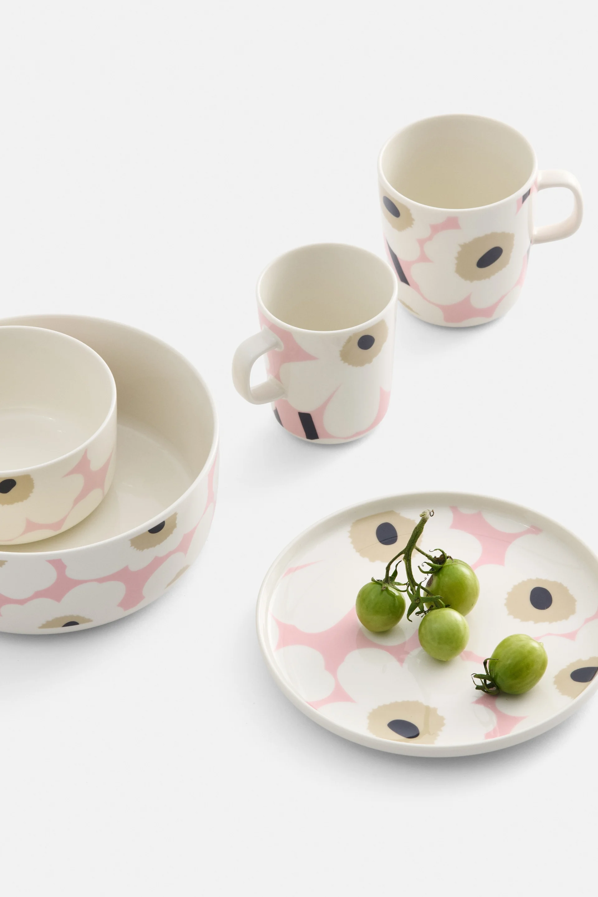 ピンクと黒の花柄が施されたクリーム色の食器。ボウル2つ、マグカップ2つ、そして緑色のミニトマトがのったプレート1つ。