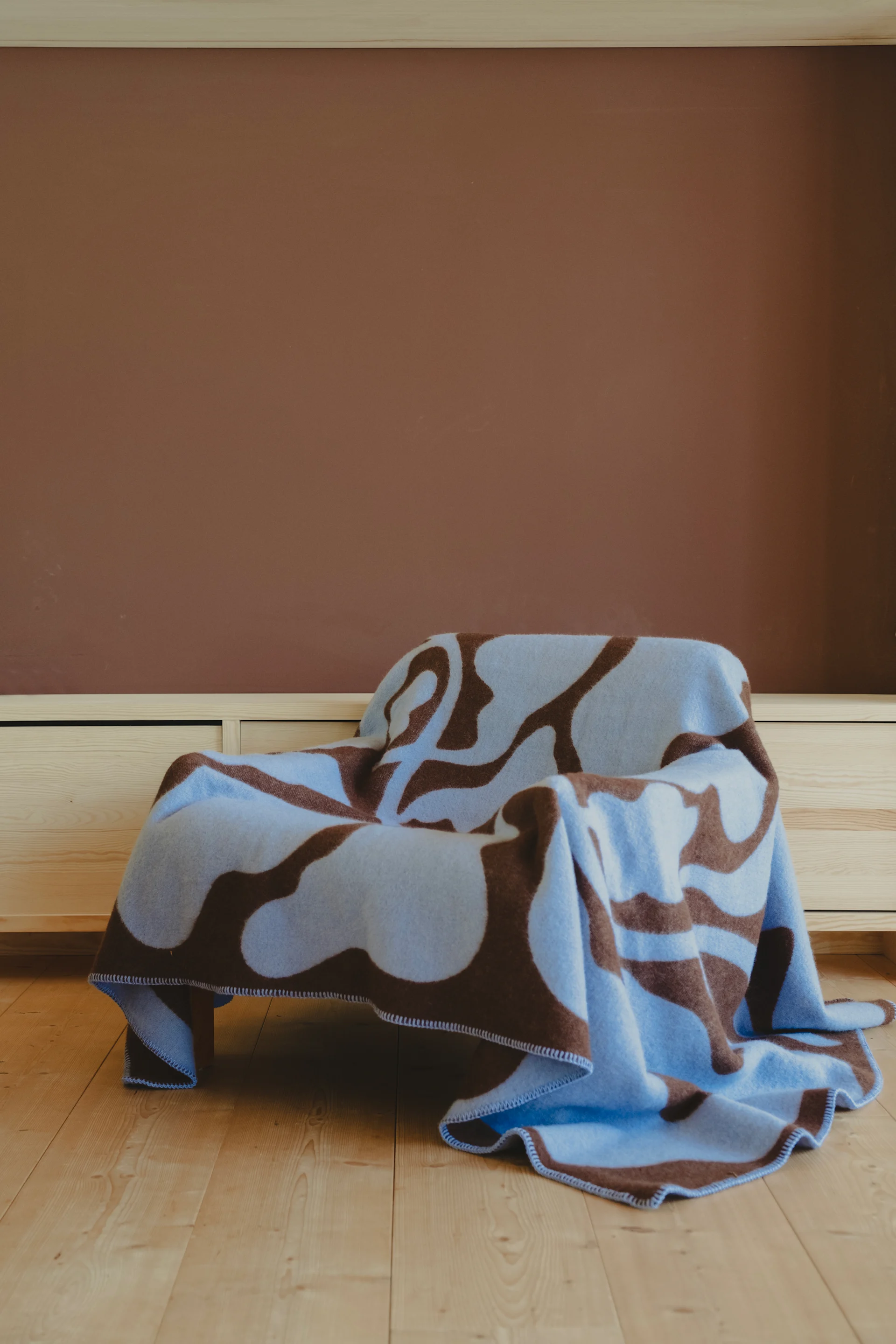 茶色の壁のある部屋で、水色と茶色のアブストラクト柄のブランケットがかけられた椅子。