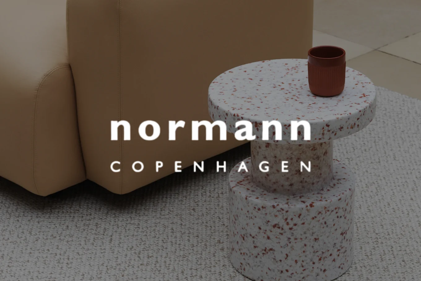 薄暗いシーンに、ランプ、暗いマグカップ、積み重ねられた本。'Audo Copenhagen'の文字が重ねられています。