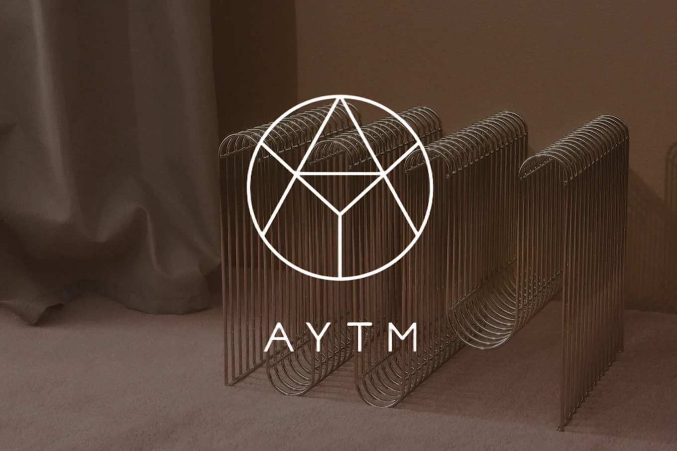 湾曲した垂直ロッドを持つモダンな金色の金属製ベンチ。白い幾何学的なAYTMロゴが表示されています。