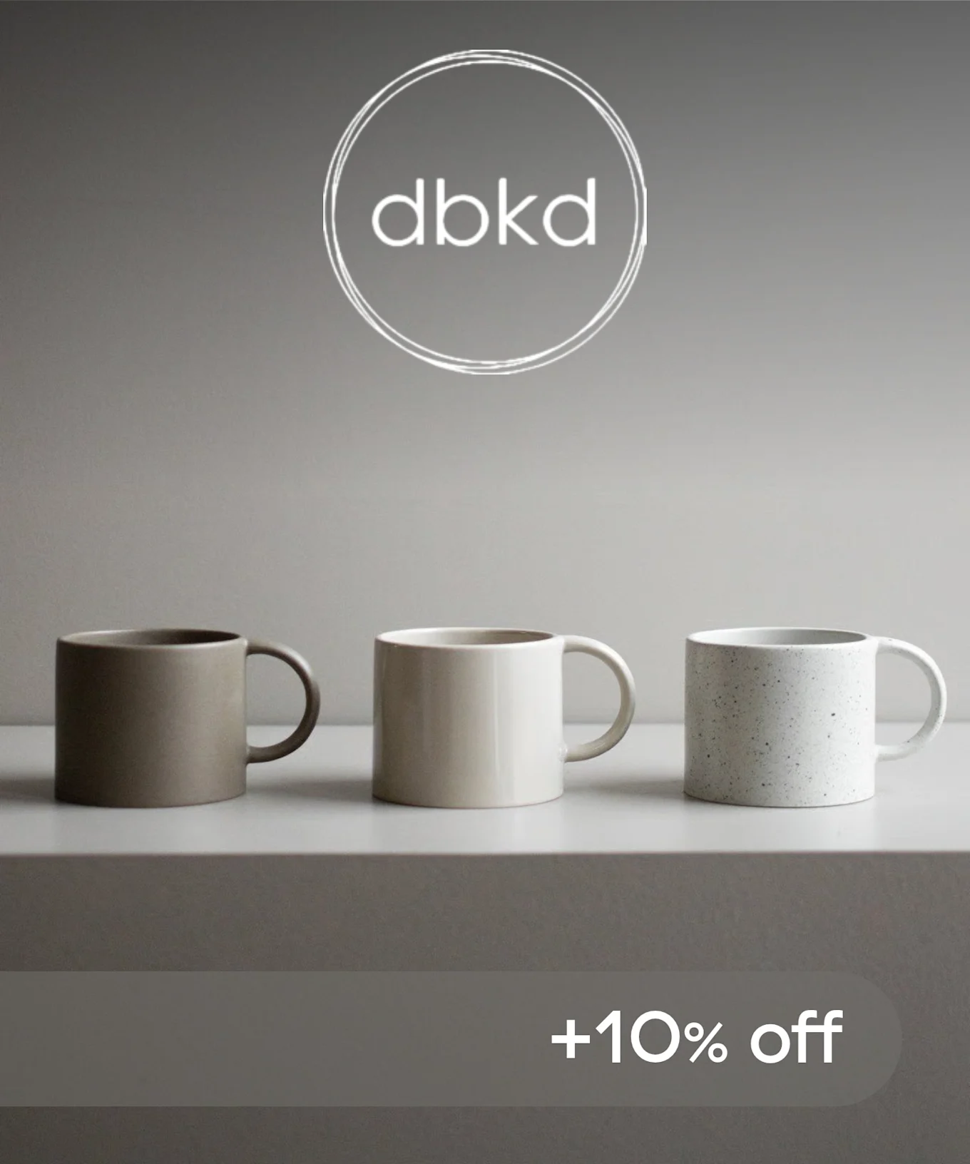 茶色、ベージュ、斑点のある白の3つのセラミックマグカップが並べられ、「dbkd」ロゴと「+10% off」の文字。