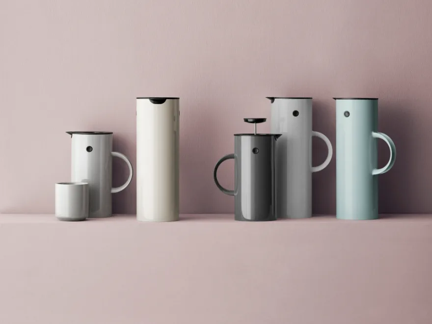 さまざまな落ち着いた色のモダンな魔法瓶とフレンチプレス、お揃いのカップがピンクの背景に。