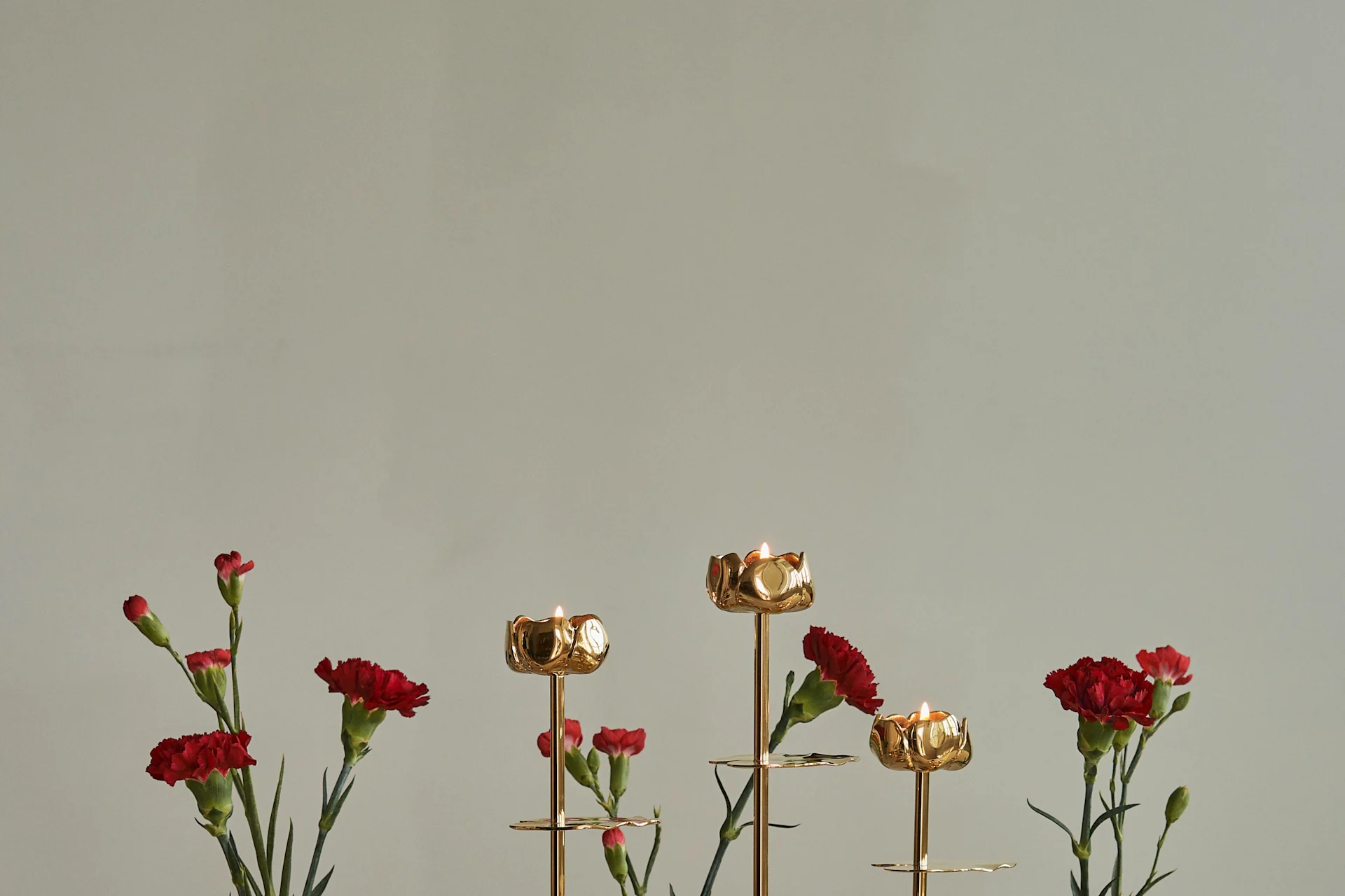 金色の花形キャンドルホルダーに火のついたキャンドルと赤いカーネーション。